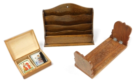 A 20thC Indian hardwood and brass inlaid book slide, carved with flowers, 33cm wide, an oak waterfall stationery rack, 30.5cm high, and a twin division playing cards box, decorated to the lid with cards, containing two packs of playing cards, 16.5cm wide.