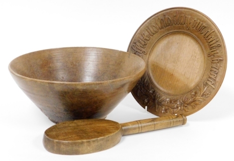 An early 20thC dough bowl, 30cm wide, an oak beater, and a wooden bread plate carved "Give Us This Day Our Daily Bread" and flowers, 26cm wide. (3)