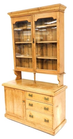 A 20thC pine dresser, the top with a moulded cornice above two glazed doors, enclosing an arrangement of shelves above a recess with a central turned column supported by two carved side supports, the base with a moulded cornice above a cupboard door flank