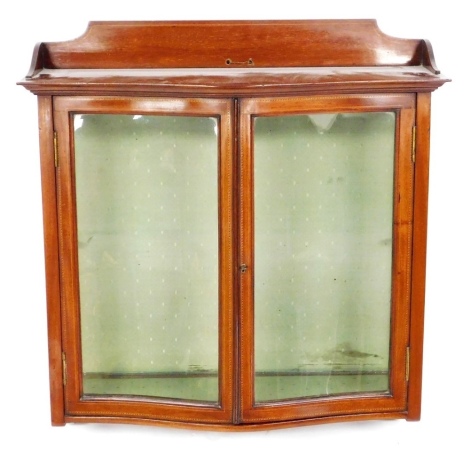 A Victorian mahogany and inlaid wall hanging display cabinet, the raised shaped back above a moulded cornice, with a pair of glazed bow fronted doors inlaid with boxwood and ebony cross banding, with a shaped base, with key, 59cm high, 60cm wide, 12cm dee