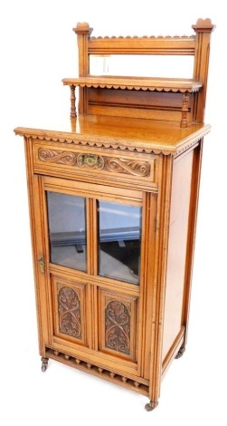 A Victorian oak side cabinet, with a carved rounded top above a bevelled mirror plate with a shelf raised on turned supports, the base with a carved scroll drawer above a door with carved and glazed panels, on castors, 144cm high, 60cm wide, 41cm deep.