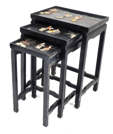 A Chinese black lacquered and hardstone inlaid nest of occasional tables, each glazed top decorated with figures in a garden, raised on square legs united by stretchers, the largest 67cm high, 49cm wide, 35cm deep.