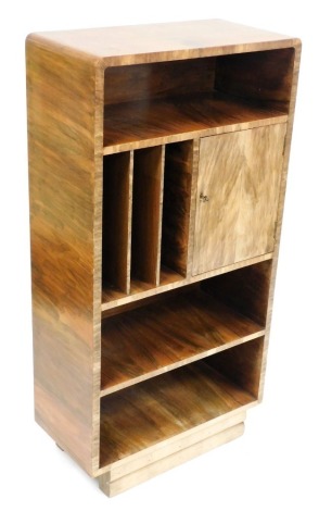 An Art Deco walnut music cabinet, the top with a central recess above a cupboard door, flanked by three compartments for records, above two book shelves, raised on a double level base, 125cm high, 62cm wide, 32cm deep.