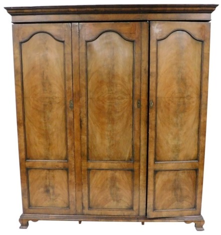 An early 20thC Georgian style mahogany triple wardrobe, the outswept pediment over three doors, enclosing hanging rails, raised on ogee bracket feet, 210cm high, 186cm wide, 62cm deep.