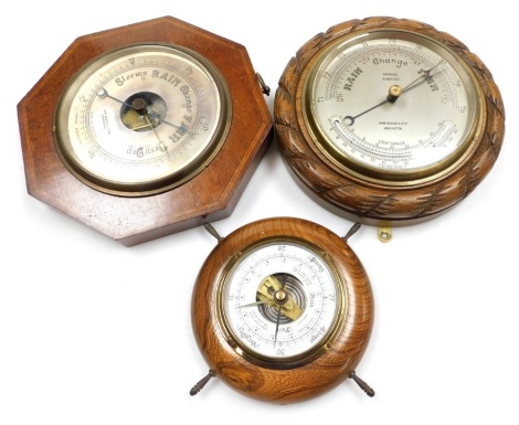 Three wall barometers, comprising a mahogany and inlaid barometer by John Barker and Co, Kensington, with a silvered dial, 24cm wide, a further oak cased barometer by John Barker and Co, 23cm diameter, together with an oak cased ship's wheel barometer, un