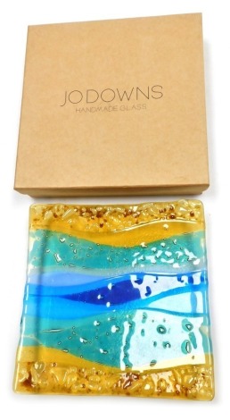 A Jo Downs hand made glass dish, of square form, decorated with flashes of amber, green, and blue glass, 22cm wide, boxed.