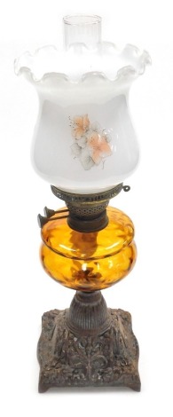 An early 20thC oil lamp, with an opaque shade decorated with flowers, an amber glass central reservoir on a cast iron base, with chimney, 58cm high.