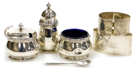 An Elizabeth II silver three piece cruet, comprising pepper pot, open salt with blue glass liner, and mustard pot with blue glass liner, each piece decorated with a band of Celtic influence, with raised roundels, Birmingham 1953, together with a EPNS spoo