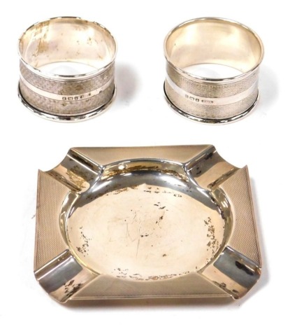 A George VI silver ashtray, with engine turned decoration, Birmingham 1948, 9cm wide, together with a pair of silver napkin rings, Birmingham 1943, 2.34oz.