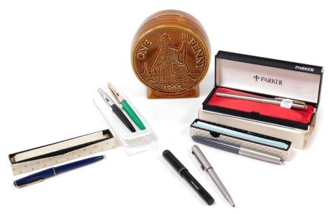 A Parker 61 Flighter Deluxe fountain pen, further fountain and ballpoint pens, and a pottery 1964 one penny money box. (a quantity)