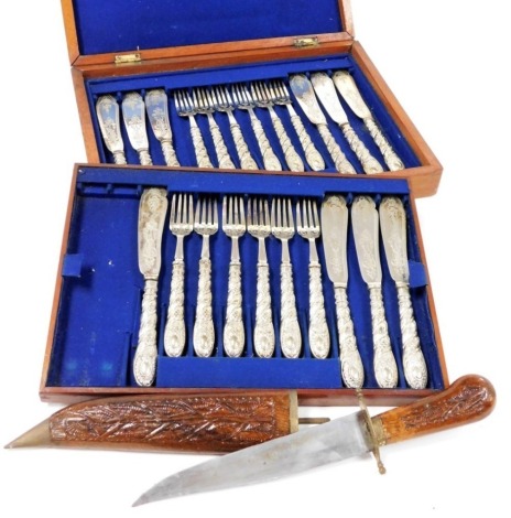 A Victorian part set of silver plated fish eaters, with engraved and embossed decoration, comprising twelve forks and ten knives, mahogany cased, together with an Indian hunting knife, in a carved wooden sheath. (2)