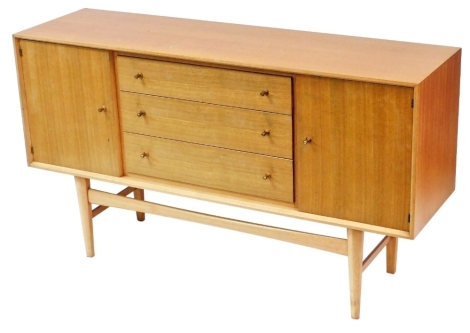 A 1950s teak sideboard, with three long drawers, flanked by a pair of cupboard doors, raised on turned legs, 86cm high, 152cm wide, 43cm deep.