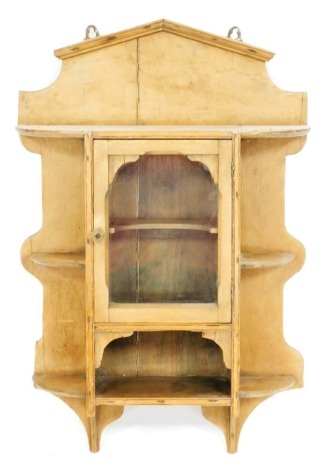 A Victorian pine hanging wall cabinet, with a central glazed door enclosing a shaped shelf, over a further shelf, flanked by four quarter shelves, 80cm high, 51cm wide.