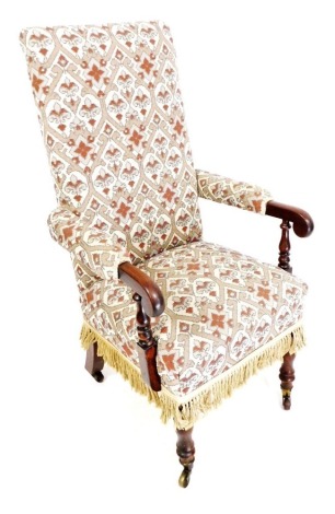 A Victorian mahogany framed high back armchair, upholstered in overstuffed floral fabric, with a tasselled fringe, raised on turned legs, brass capped on castors, 63cm wide.