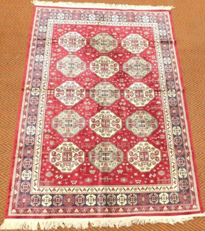 A Turkoman silk red ground rug, decorated with fifteen central medallions, animals and motifs, within repeating floral borders, 192cm x 140cm.