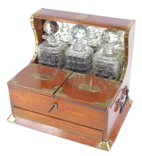 A Victorian oak Tantalus, with brass bound shield and sides, with three cut glass decanters and stoppers, and a two lidded compartment with single drawer, brass swing carry handles, 36cm high, 35cm wide, 25cm deep.