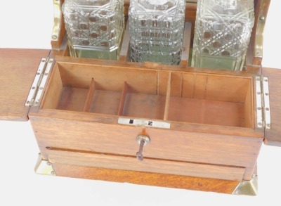 A Victorian oak Tantalus, with brass bound shield and sides, with three cut glass decanters and stoppers, and a two lidded compartment with single drawer, brass swing carry handles, 36cm high, 35cm wide, 25cm deep. - 3