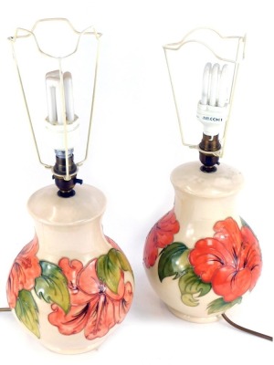 A pair of Moorcroft Hibiscus pattern table lamps, each on a cream ground, stamped to underside, with shades, 48cm high. (2)