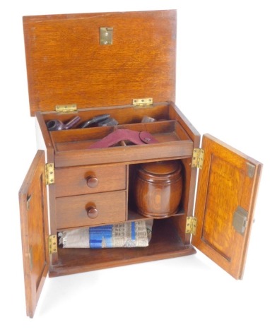 An early 20thC oak smoker's cabinet, of plain form with two single doors and swing lid bearing crest, Presented as a Token of Esteem to WB Crookes by The Tinsley U.M.I.F.C, June 23rd 1921, contents including oak barrel tobacco jar, two internal fitted dra