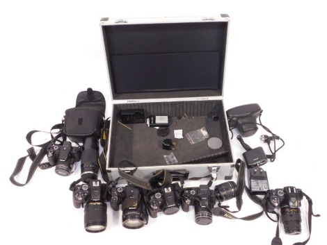 A group of cameras and camera equipment, comprising a Nikon Coolpix P520, a Nikon Coolpix P900, Nikon AF-PDX18-50mm lens, an Asahi Pentax camera, a Nikon Coolpix P610, Nikon Coolpix D5300, with Nikon DXVR 18-140mm lens, a Nikon Cosina number 58 lens, a Ni