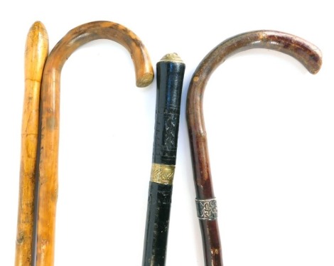 Four walking sticks, comprising a ebonised and brass capped swagger stick, a silver collared walking stick, and two turned wooden walking sticks, 83cm long. (4)