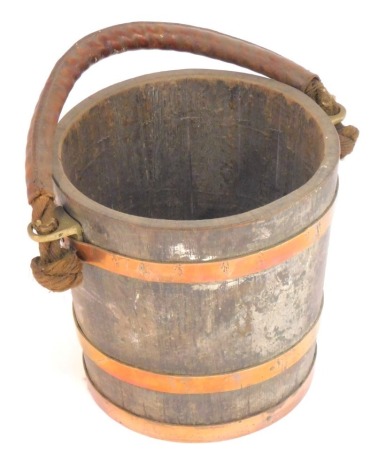 A 19thC elm milking bucket, with a rope and leather handle, with brass strapwork, stamped Bucket M6552, 30cm high, 32cm diameter.