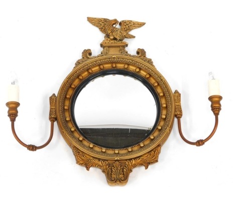 A gilt girandole mirror in Regency style, with an eagle crest, and bow and feather detail, with convex mirror and two candle branches, 66cm high, 72 cm wide, 13cm deep