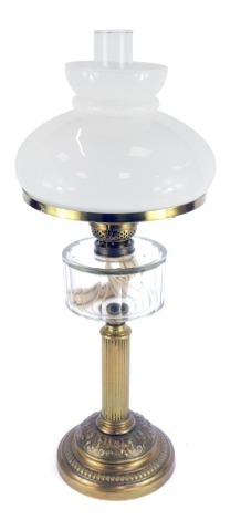 An early 20thC brass oil lamp, with a shaped white glass shade and funnel, with glass reservoir on a brass fluted stem, with vine and berry base, on a circular foot, 70cm high.