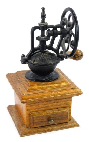 A French vintage cast iron coffee grinder, with a wheel turning handle, raised on an oak base with single drawer, 28cm high.