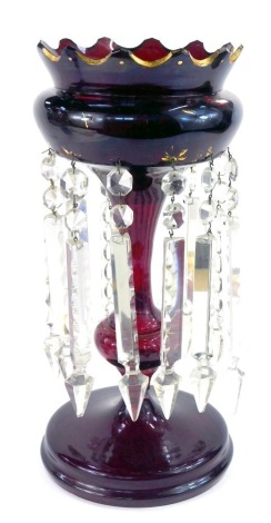 A late 19thC ruby glass lustre, with fluted glass top, with gilt highlights, on a stepped foot, with clear prismatic drops, 43cm high.