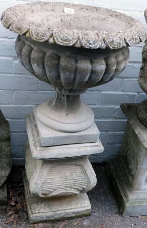 A reconstituted stone garden urn, semi fluted circular form, on a square base, on shaped plinth, 84cm high.