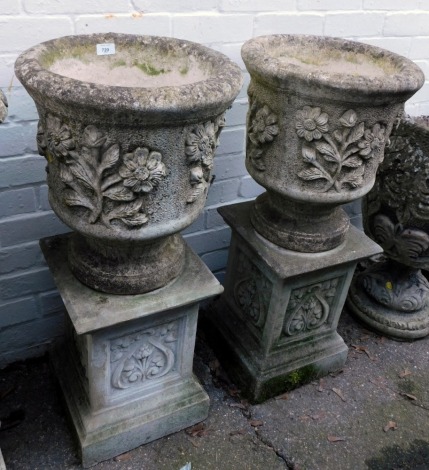 A pair of reconstituted stone garden planters, each with a circular planter with floral design, on a square set base with floral panels, 89cm high, 40cm diameter.