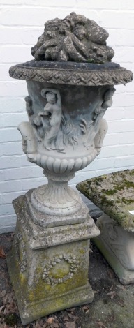 A reconstituted stone garden urn, with fruits and flowers top, of campana form with relief moulded figures of semi nude females, on a square wreathed plinth, 120cm high.