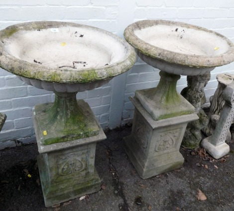 A pair of reconstituted stone garden urns, each with a fluted top, on a square foliate decorated plinths, 88cm high, 60cm diameter.