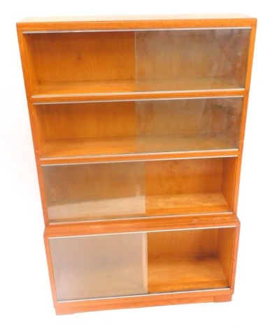 A mid century light oak modular bookcase, of four sections, with glass sliding doors, raised on a plinth base, 135cm high, 90cm wide, 29cm deep.