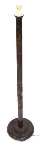 An early 20thC Eastern hardwood standard lamp, carved with buildings and trees, the cylindrical column raised on a stepped circular base, 170cm high. WARNING! This lot contains untested or unsafe electrical items. It is supplied for scrap or re-conditio