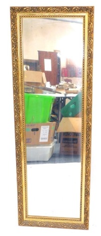 A rectangular gilt framed wall mirror, decorated with foliate scrolls, 113cm x 37.5cm.