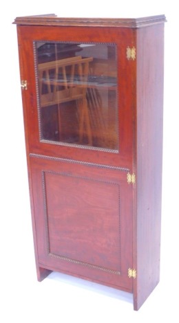 An early 20thC mahogany and oak cupboard bookcase, the glazed and panelled door opening to reveal shelves, raised on rectangular side supports, 127cm high, 58cm wide, 29cm deep.