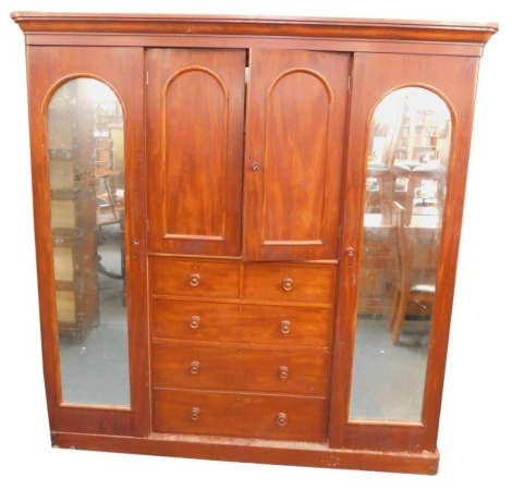 A Victorian mahogany compactum wardrobe, the out swept pediment over a pair of doors enclosing two shelves, above two short over three long drawers, flanked by a pair of cupboard doors inset domed glass, opening to reveal a single shelf over hanging hooks