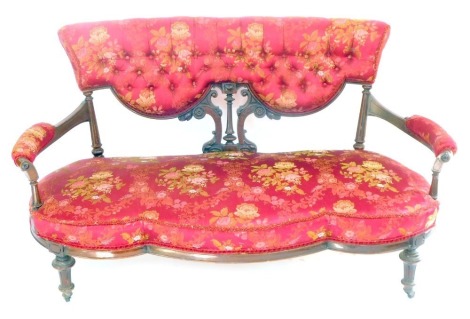 A Victorian walnut serpentine show frame two seater sofa, upholstered in button back red and floral decorated fabric, overstuffed seat, with scrolling arms, raised on turned legs, brass capped on castors, 156cm wide.