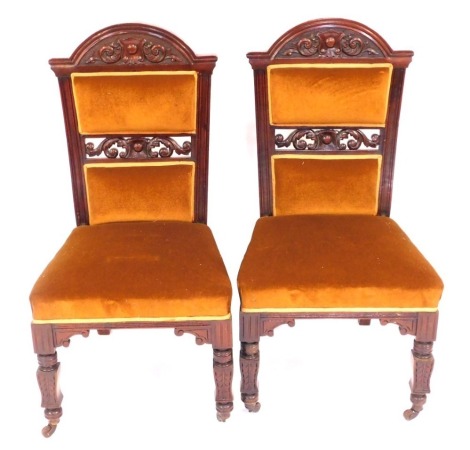 A pair of Victorian mahogany salon chairs, with mustard over stuffed upholstery, on turned legs, brass capped on castors.