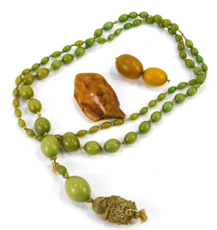 A mixed group of coloured jewellery, comprising a green necklace, with knotted string, and pendant drop, 84cm long, 39.2g all in, a Baltic rough piece, 5.5cm wide, 14.2g all in, and two butterscotch style amber beads, 11.6g all in. (3)