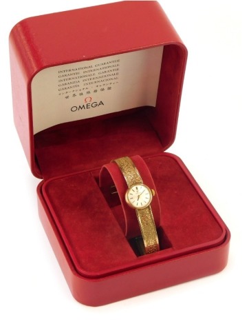 An Omega 9ct gold lady's wristwatch, with small silvered dial, 1.5cm wide, on bark effect bracelet, 20cm long, 20.4g all in, in Omega box.