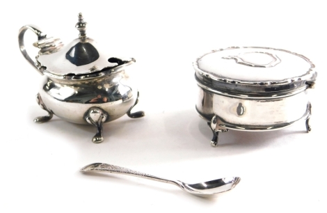 A George V silver mustard pot, with shaped lid, urn finial, plain ear handle, on quadruple hoof feet, London 1916, with associated spoon, and a silver and part embroidered material box, 5.6oz all in.