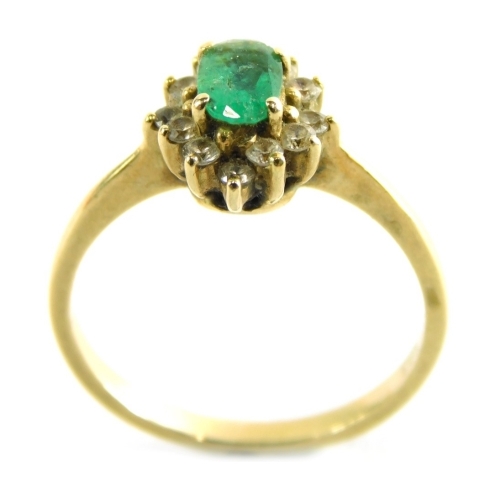 An emerald and diamond cluster ring, with pale green oval emerald in claw setting surrounded by twelve tiny diamonds, on a yellow metal band unmarked, stamped T.93, ring size M, 2.8g all in.