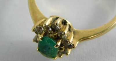 An emerald and diamond cluster ring, with pale green oval emerald in claw setting surrounded by twelve tiny diamonds, on a yellow metal band unmarked, stamped T.93, ring size M, 2.8g all in. - 2