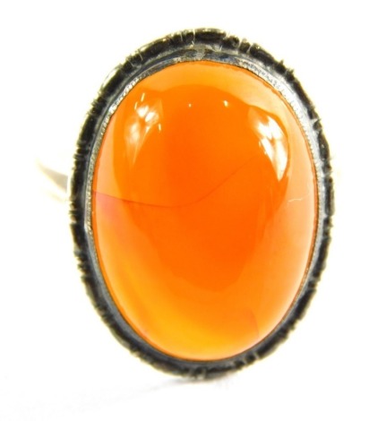 An orange agate dress ring, with cabochon stone in white metal band, unmarked, ring size M½, 3.7g all in.