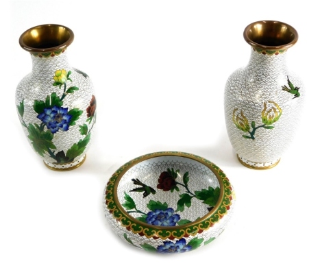Three items of oriental cloisonne, a pair of vases and bowl, each profusely decorated with flowers and exotic birds, on white and gilt highlighted ground, the vase 21cms high. (3)