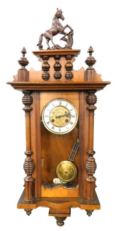 An early 20thC walnut Vienna wall clock, with heavily carved horse finial flanked by urns, above a 13cm diameter Roman numeric dial, with fancy raised leaf centre, in a three part glazed case flanked by quarter columns, with eight day movement and pendulu