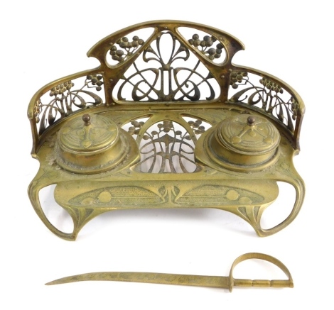 An early 20thC Art Nouveau brass ink stand, with pierced galleried back, two fixed inkwells, front space for pens, 26cm wide, and an associated sword paperknife.